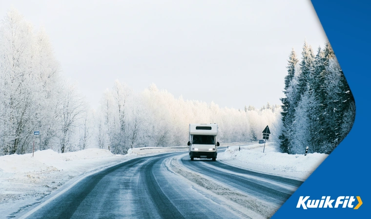 a motorhome drives carefully along a frozen road � the trees alongside are all covered in snow in front of an almost-white sky.